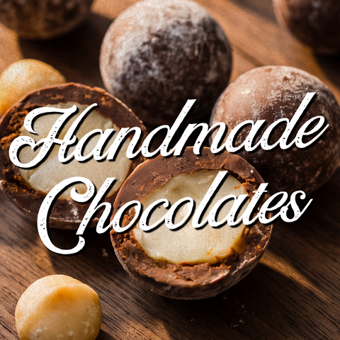 A close-up arrangement of assorted chocolates on a wooden surface, including whole dark chocolate truffles and one cut open to show a creamy white filling. Large white script text reading 'Handmade Chocolates' overlays the center.
